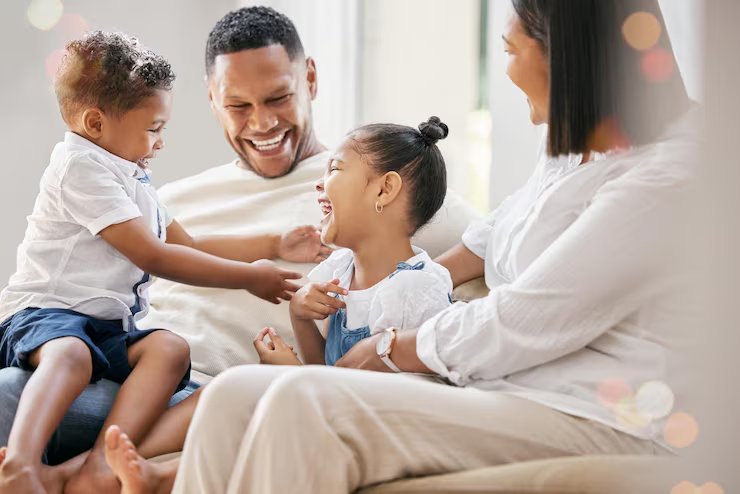Pai e mãe brincando no sofá com filho e filha pequenos